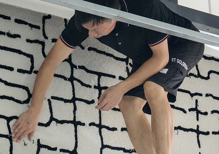 A professional tufted rug artisan is checking the texture of a semi-finished cream tufted wool rug on the backing cloth frame