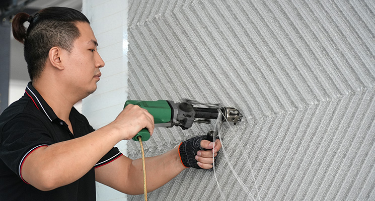 A skilled hand tufting artisan producing an abstract beige woolen rug, using a green professional tufting gun