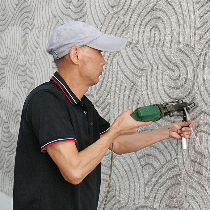 A skilled artisan in black uniform tufting a beige abstract custom large wool rug, using a green professional tufting gun