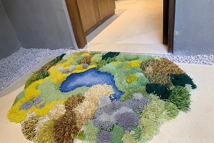 A hand tufted woolen green moss rug with an abstract lake and forest pattern design, in front of an entrance door