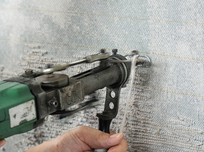 A professional rug tufting worker is producing a light gray tufted area rug, with rapid pushing and punching