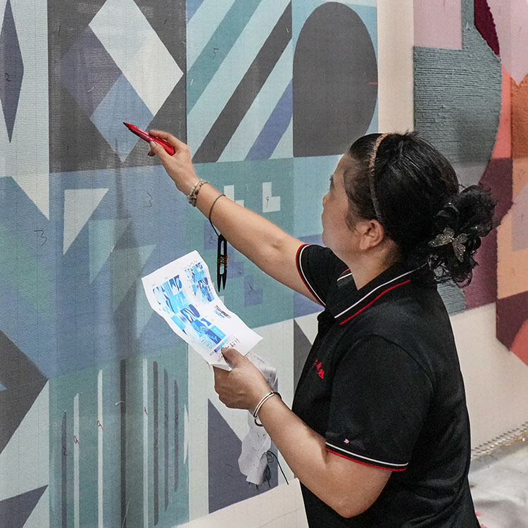 A hand tufting artisan is marking geometric patterns on the backing cloth of a custom tufted wool rug