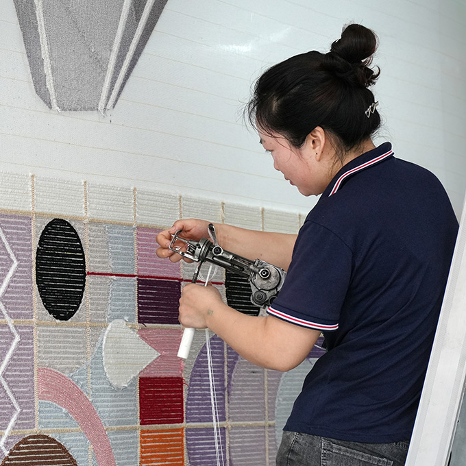 A young hand tufting lady preparing the yarn for a Bauhaus style custom woolen rug, holding the professional electrical tufting gun with one hand