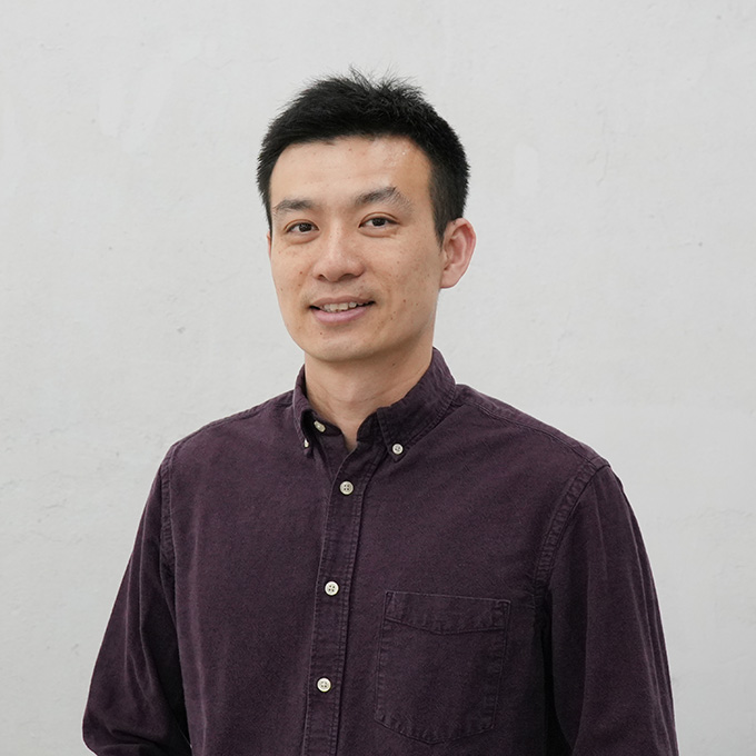 The business manager of custom hand tufted rug company, wearing a brown shirt, smiling in front of a white wall