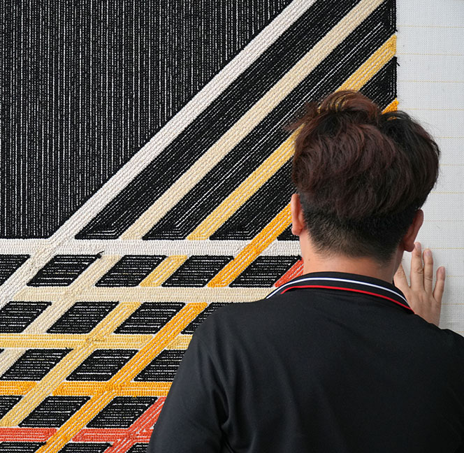 A hand tufting artisan checking quality of a black custom rug with simple abstract lines for homes