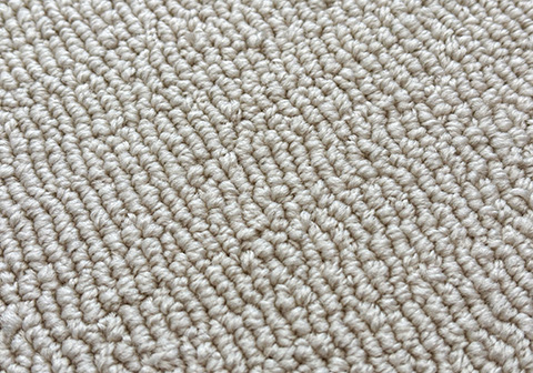 Beige loop-pile tufted rug texture displaying uniform, uncut yarn loops creating a distinctive ribbed pattern