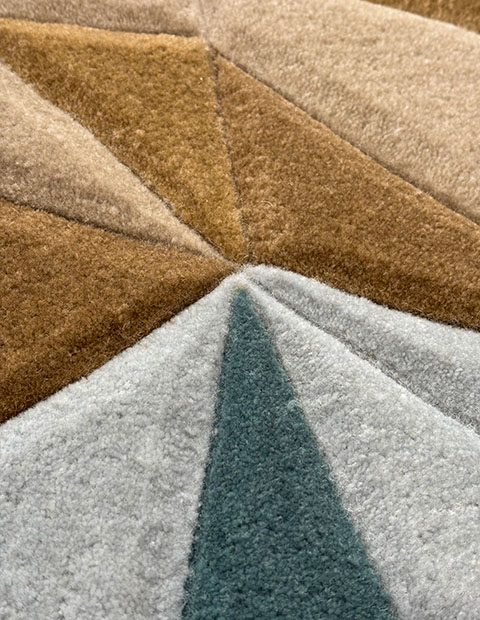 Tufted rug with deeply carved channels forming angular geometric design in brown, grey, and teal cut pile texture