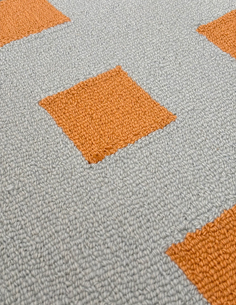 Loop-pile tufted rug featuring orange square accents on grey background, showcasing uniform loop texture throughout