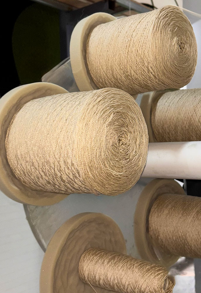 Spools of beige yarn mounted on tufting rack for rug production