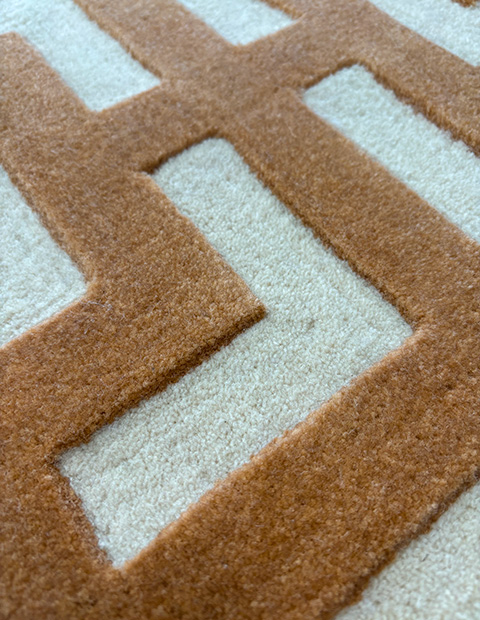 Tufted rug pattern featuring high and low cut pile contrast with caramel brown geometric lines on cream background