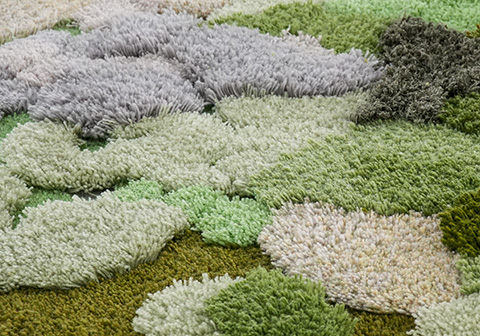 Tufted moss rug texture showing plush New Zealand wool yarns in multiple pile heights, featuring soft gray, sage, and olive green