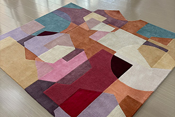 Custom hand tufted rug with Bauhaus inspired geometric circles, triangles and squares in solid colors on a beige floor