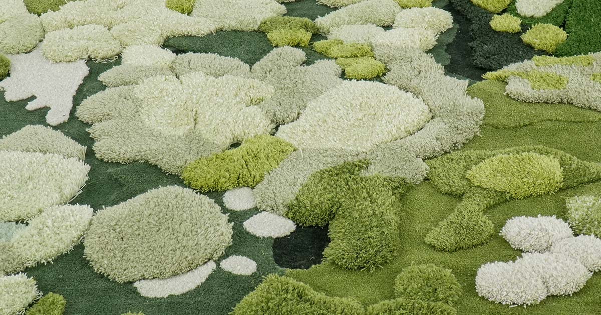 An overhead shot of a moss-inspired tufted rug in varied pile heights. The rug features organic white, light green, and dark green forms to provide a three-dimensional appearance similar to a stylized moss garden.