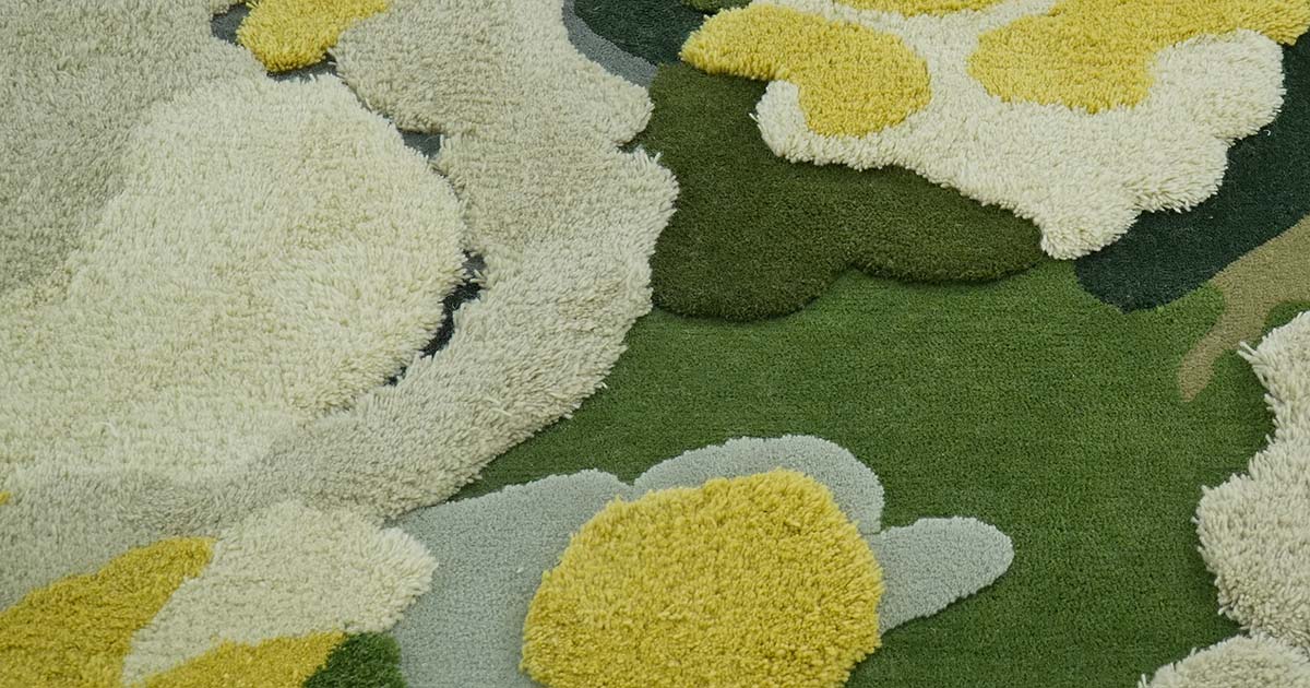Close-up of a custom tufted rug having an organic design showcasing white, yellow, and different green circular patterns. The rug consists of varying pile heights with a textured, moss-like quality.